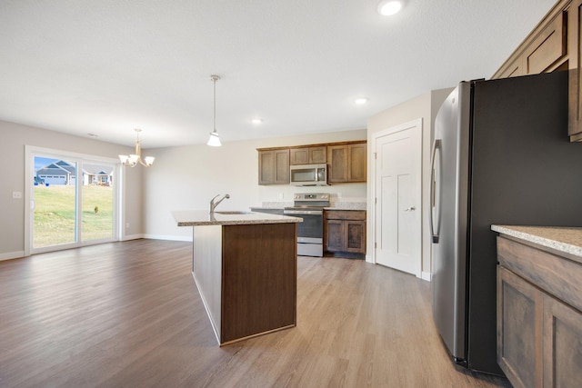 kitchen with hanging light fixtures, light stone counters, a chandelier, appliances with stainless steel finishes, and light wood-type flooring