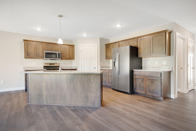 kitchen with light stone counters, hanging light fixtures, stainless steel appliances, and light wood-type flooring