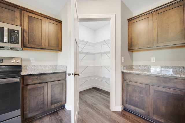 kitchen with hardwood / wood-style floors, light stone countertops, a textured ceiling, and appliances with stainless steel finishes