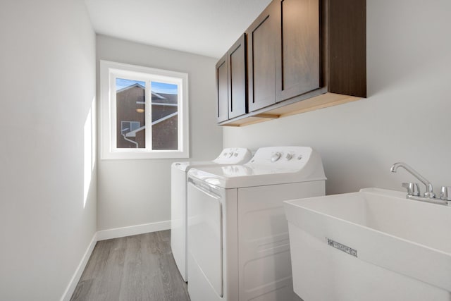 clothes washing area with washing machine and clothes dryer, sink, cabinets, and light wood-type flooring