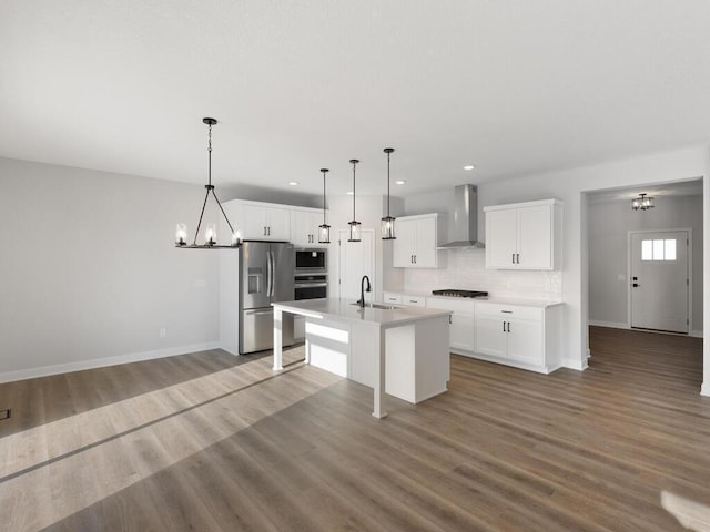 kitchen featuring appliances with stainless steel finishes, a kitchen island with sink, wall chimney range hood, and white cabinets