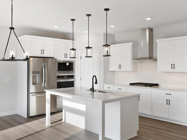 kitchen with decorative light fixtures, an island with sink, sink, stainless steel appliances, and wall chimney exhaust hood