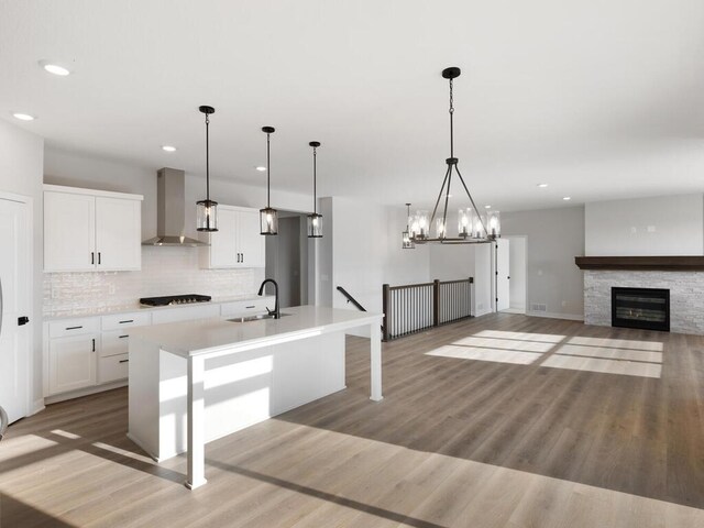 kitchen featuring wall chimney exhaust hood, a center island with sink, pendant lighting, black gas cooktop, and white cabinets