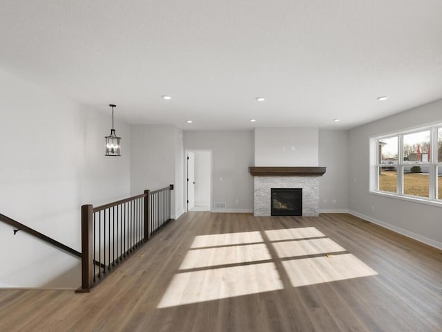 unfurnished living room featuring a stone fireplace, a notable chandelier, and light wood-type flooring