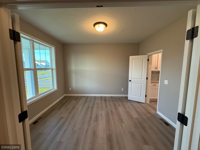 unfurnished room with light wood-type flooring, a textured ceiling, and a wealth of natural light