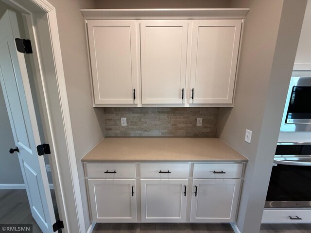 interior space featuring backsplash, dark hardwood / wood-style flooring, white cabinets, and appliances with stainless steel finishes