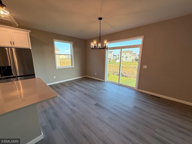 unfurnished dining area featuring a textured ceiling, dark hardwood / wood-style floors, and an inviting chandelier