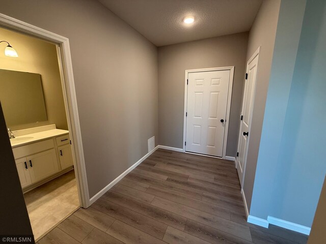 hall with light hardwood / wood-style flooring, a textured ceiling, and sink