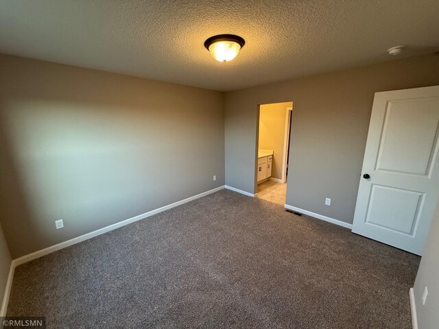 unfurnished bedroom featuring connected bathroom, light carpet, and a textured ceiling