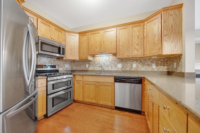 kitchen featuring sink, stainless steel appliances, light stone counters, backsplash, and light wood-type flooring