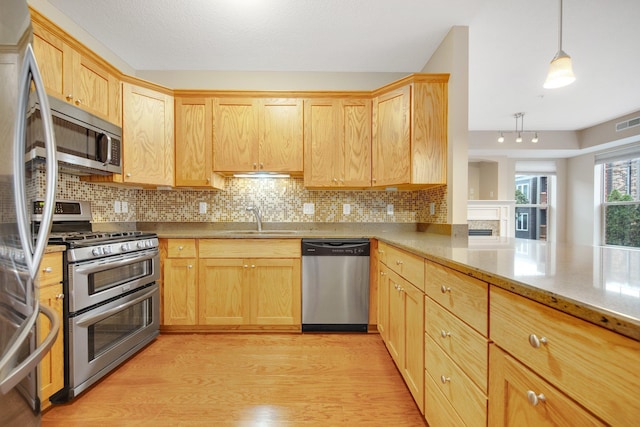 kitchen with backsplash, sink, hanging light fixtures, light hardwood / wood-style floors, and stainless steel appliances