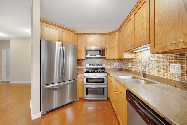 kitchen with appliances with stainless steel finishes, light wood-type flooring, backsplash, light stone counters, and sink