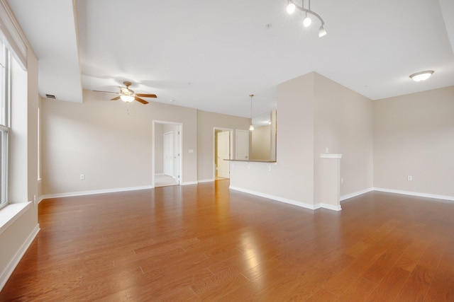 empty room featuring a healthy amount of sunlight, ceiling fan, and wood-type flooring