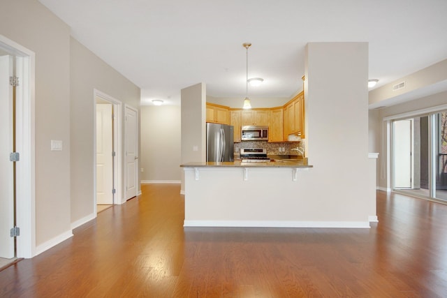 kitchen with hanging light fixtures, dark hardwood / wood-style floors, light brown cabinetry, kitchen peninsula, and stainless steel appliances