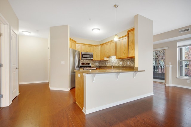 kitchen featuring pendant lighting, dark wood-type flooring, appliances with stainless steel finishes, kitchen peninsula, and a breakfast bar area