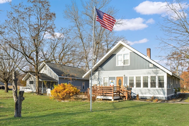 rear view of property featuring a sunroom, a yard, and a wooden deck