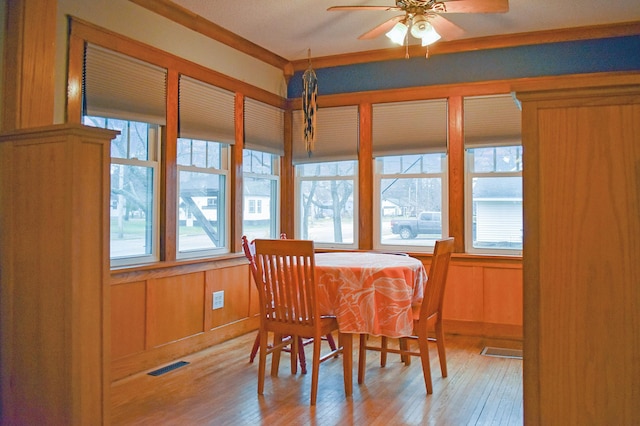 dining area with ornamental molding, light hardwood / wood-style floors, ceiling fan, and wooden walls