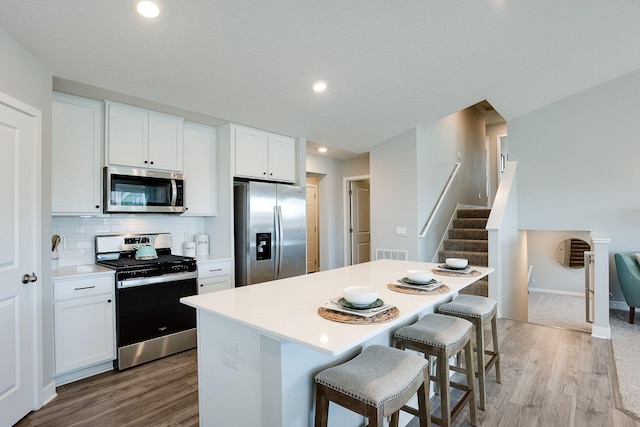 kitchen with tasteful backsplash, appliances with stainless steel finishes, a breakfast bar area, white cabinets, and light wood-type flooring