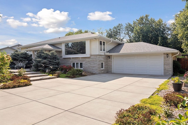 split level home featuring stone siding, fence, roof with shingles, concrete driveway, and an attached garage