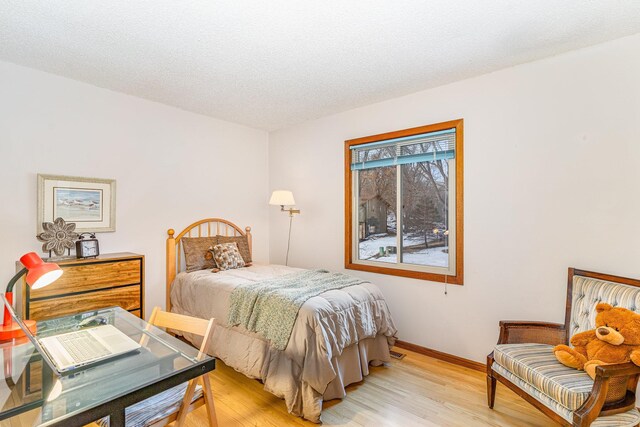 bedroom featuring a textured ceiling, light wood-type flooring, and baseboards