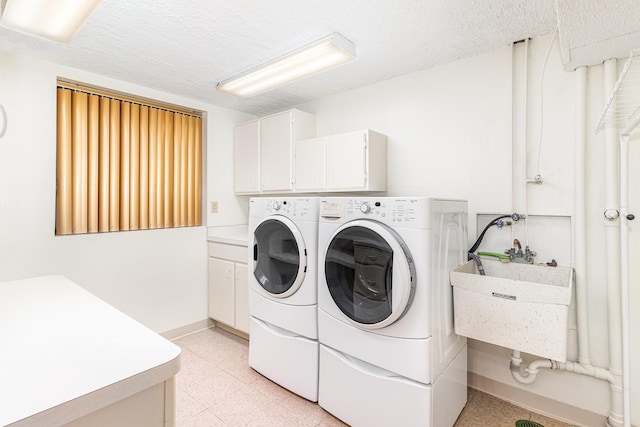 washroom featuring a sink, a textured ceiling, cabinet space, light floors, and washing machine and clothes dryer