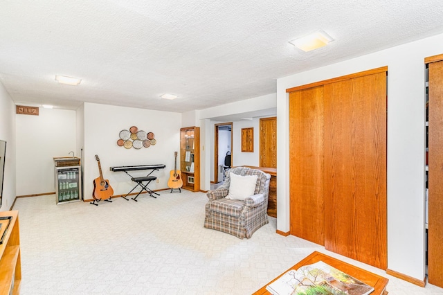 sitting room featuring wine cooler, light colored carpet, a textured ceiling, and baseboards