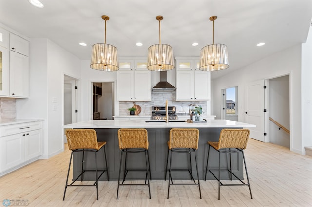 kitchen featuring white cabinets, light hardwood / wood-style floors, wall chimney exhaust hood, and an island with sink