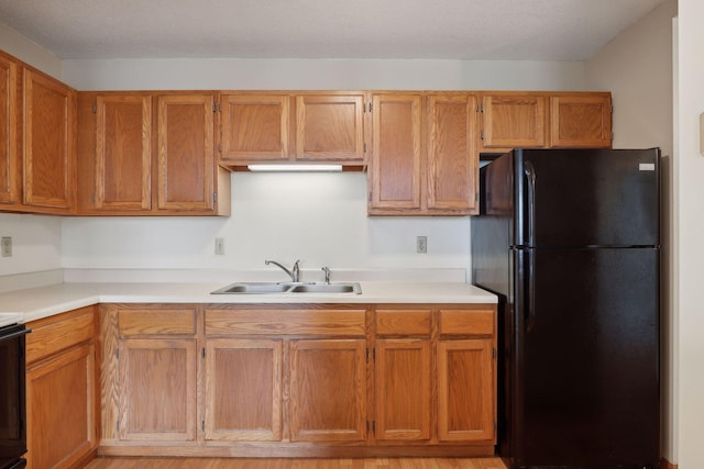 kitchen featuring a textured ceiling, black refrigerator, light wood-type flooring, and sink