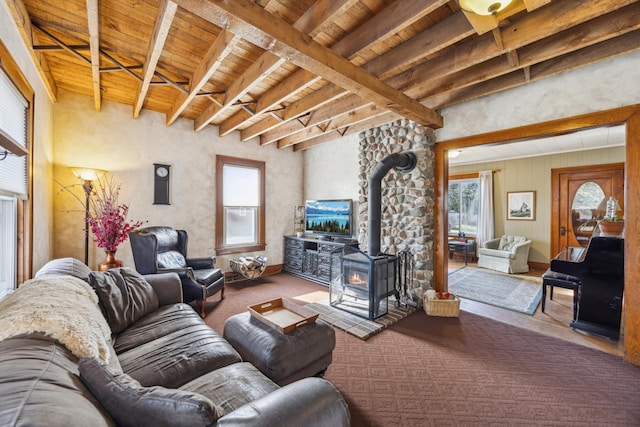 living room with beamed ceiling, carpet flooring, a wood stove, and wood ceiling