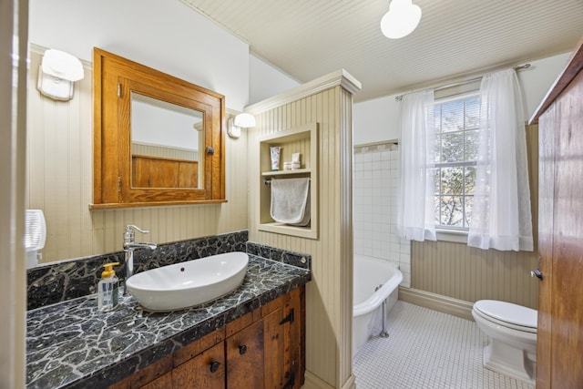 bathroom featuring a bathtub, wood walls, vanity, tile patterned flooring, and toilet