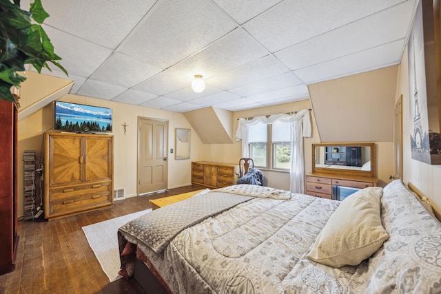 bedroom with a paneled ceiling, wood walls, and dark wood-type flooring