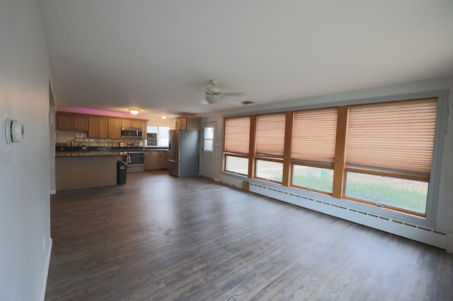 unfurnished living room with dark hardwood / wood-style floors, ceiling fan, a wealth of natural light, and a baseboard heating unit