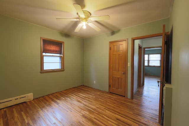 empty room with hardwood / wood-style floors, ceiling fan, and a baseboard heating unit