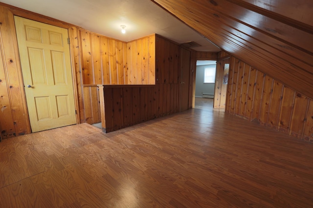 additional living space with wooden walls, hardwood / wood-style floors, a baseboard radiator, and lofted ceiling