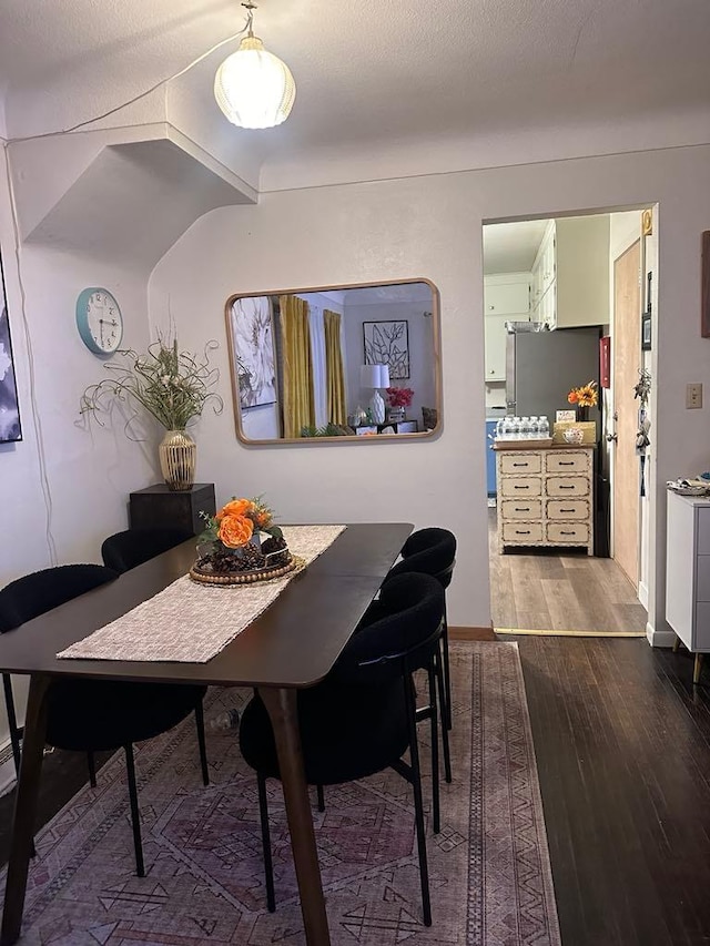 dining space with lofted ceiling, a textured ceiling, and hardwood / wood-style flooring