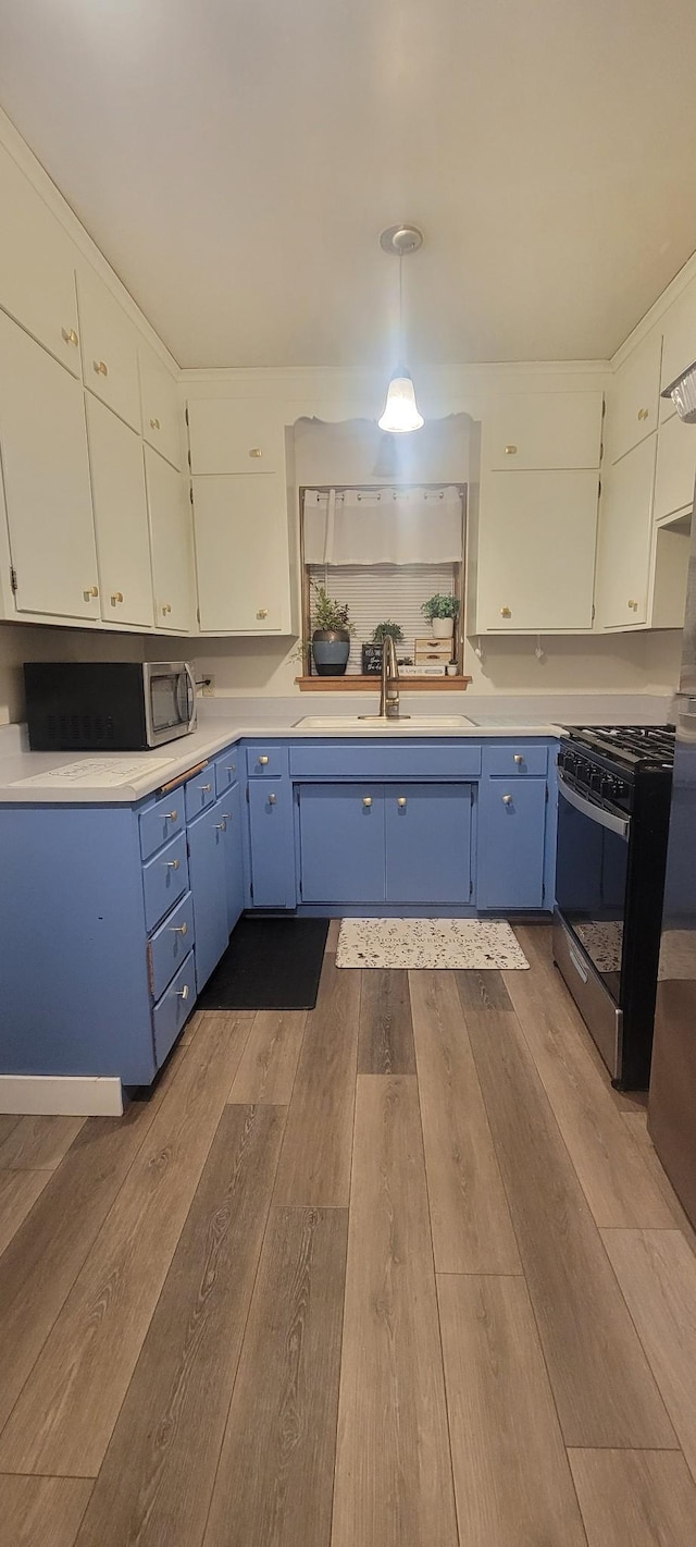 kitchen with stainless steel gas range, sink, wood-type flooring, pendant lighting, and white cabinetry