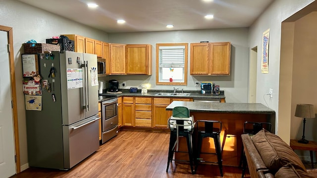 kitchen with sink, stainless steel appliances, light wood-type flooring, and a breakfast bar area