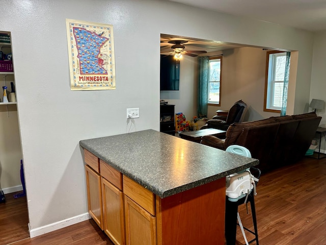 kitchen with kitchen peninsula, dark wood-type flooring, ceiling fan, and a breakfast bar