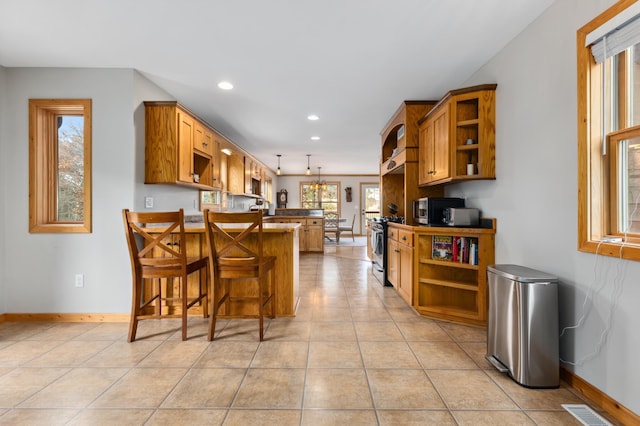 kitchen featuring kitchen peninsula, a breakfast bar, gas stove, pendant lighting, and light tile patterned floors