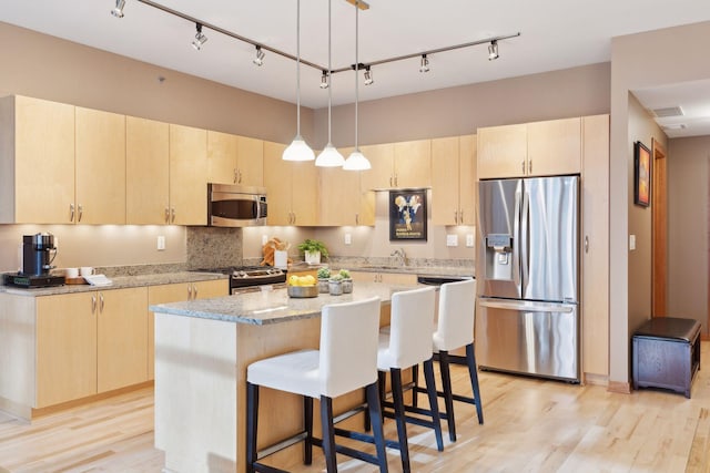 kitchen featuring light stone countertops, appliances with stainless steel finishes, light brown cabinets, decorative light fixtures, and a kitchen island