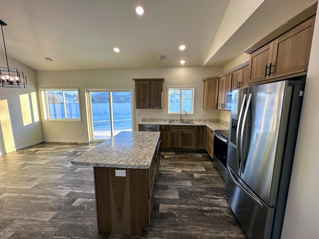 kitchen with appliances with stainless steel finishes, light stone counters, sink, a center island, and hanging light fixtures