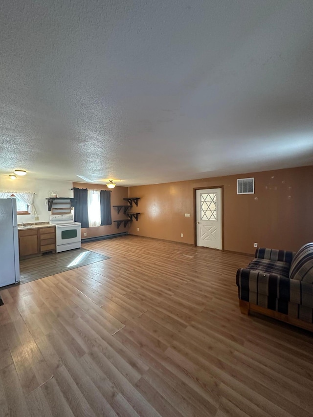 unfurnished living room with a baseboard heating unit, wood finished floors, visible vents, and a textured ceiling