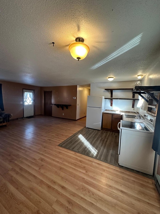 kitchen with wood finished floors, freestanding refrigerator, a sink, stove, and a textured ceiling