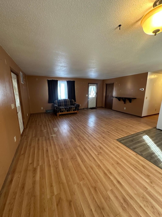 unfurnished living room with light wood finished floors, baseboard heating, a textured ceiling, and visible vents