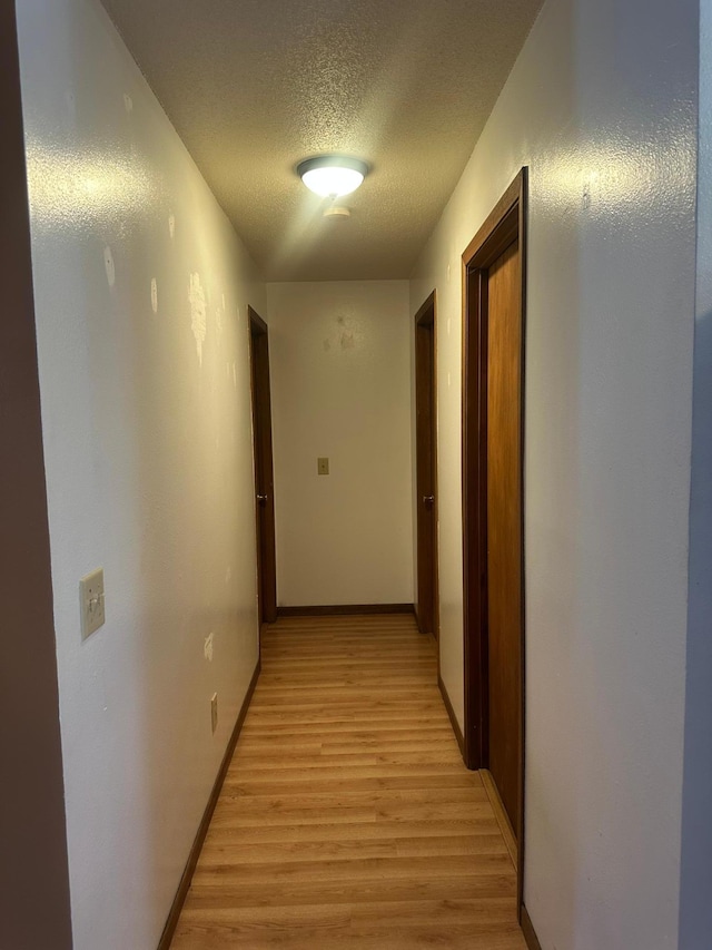 hall with light wood-type flooring, baseboards, and a textured ceiling