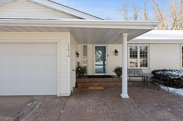 snow covered property entrance featuring a garage and a porch