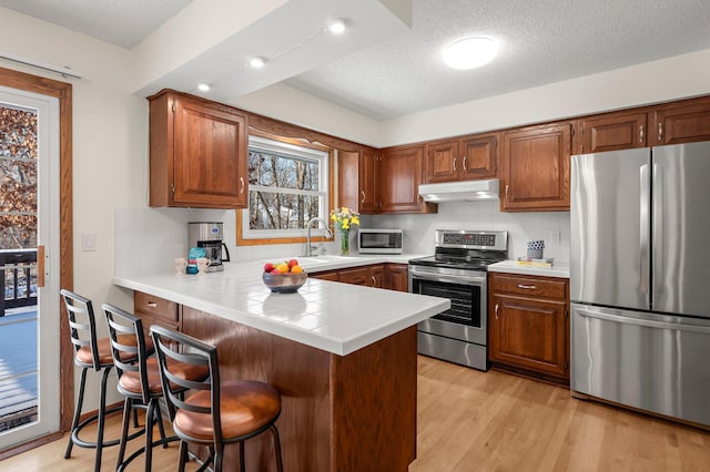 kitchen featuring stainless steel appliances, sink, light hardwood / wood-style flooring, kitchen peninsula, and decorative backsplash