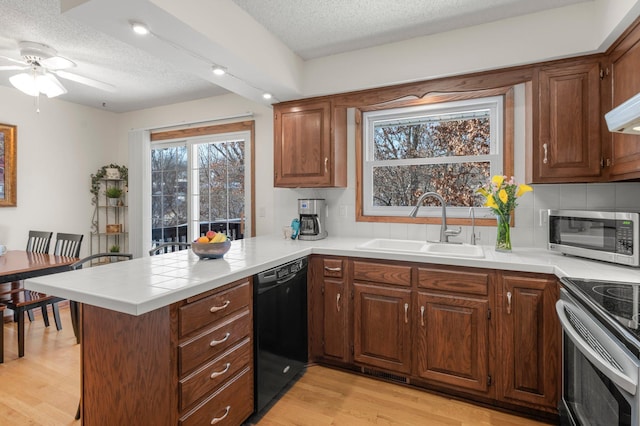 kitchen featuring stainless steel appliances, sink, a textured ceiling, light wood-type flooring, and kitchen peninsula