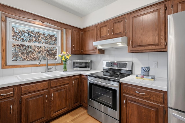 kitchen with a textured ceiling, stainless steel appliances, light hardwood / wood-style floors, backsplash, and sink