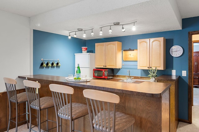 kitchen with kitchen peninsula, a textured ceiling, white refrigerator, light brown cabinetry, and sink